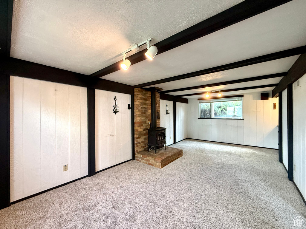 Unfurnished living room with a wood stove, wood walls, beamed ceiling, a textured ceiling, and carpet
