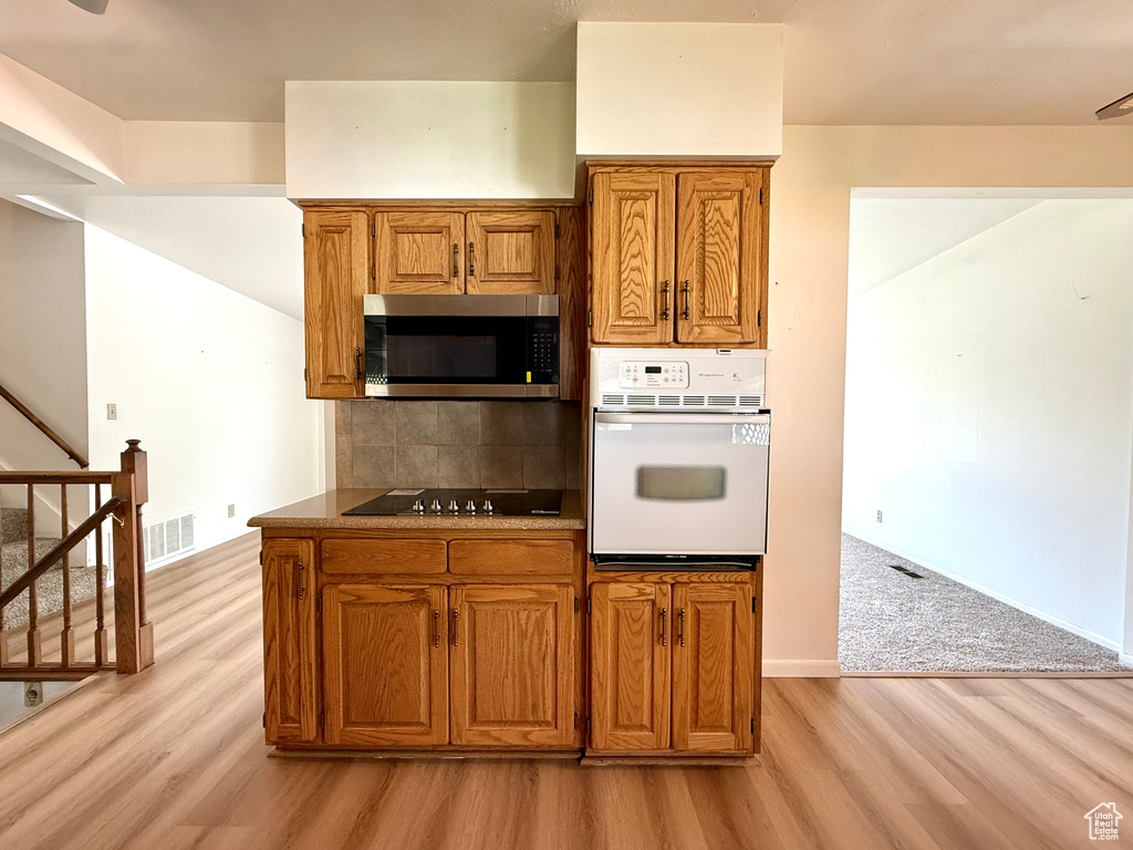 Kitchen featuring brown cabinetry, white oven, stainless steel microwave, black electric stovetop, and light wood-style floors