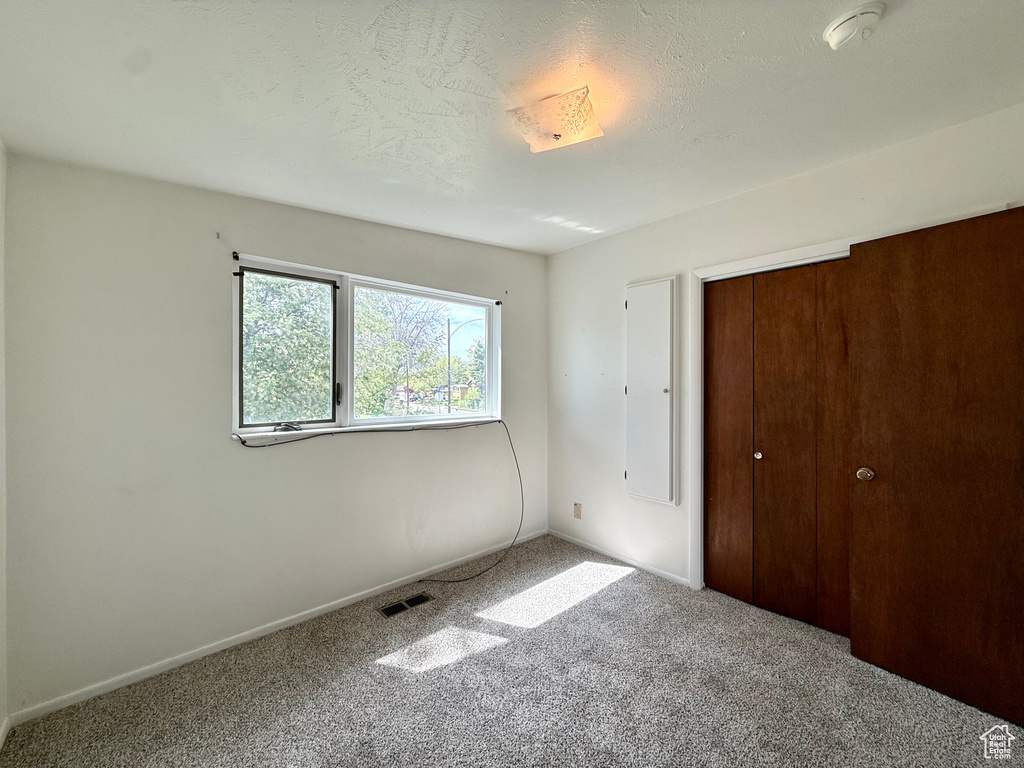 Unfurnished bedroom with a textured ceiling, visible vents, carpet floors, baseboards, and a closet