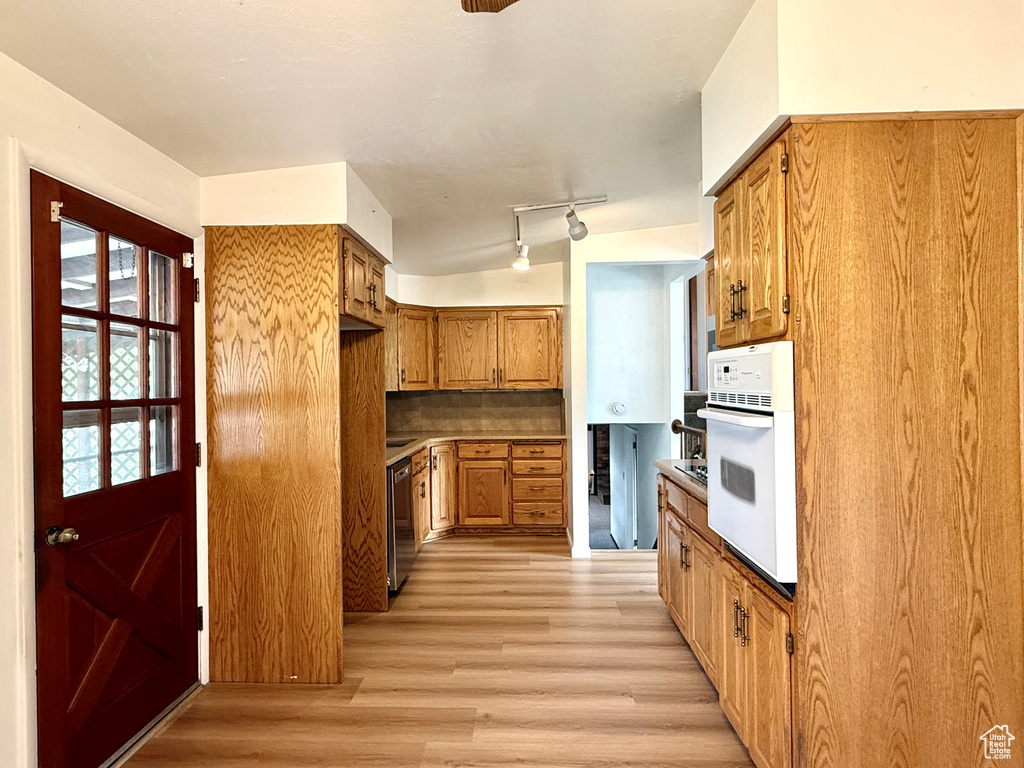 Kitchen featuring brown cabinets, light wood finished floors, dishwasher, decorative backsplash, and white oven
