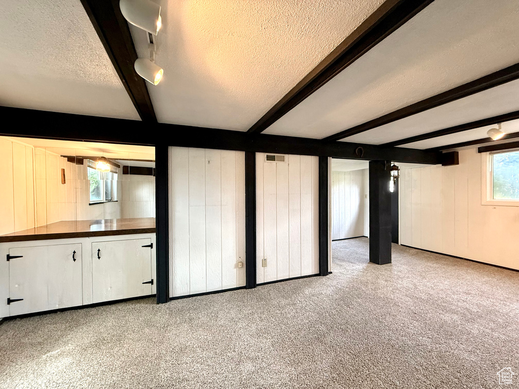 Unfurnished living room with carpet, beam ceiling, a textured ceiling, and visible vents