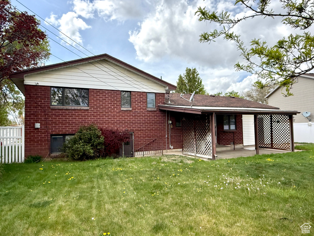 Back of property with a lawn, brick siding, fence, and a patio area