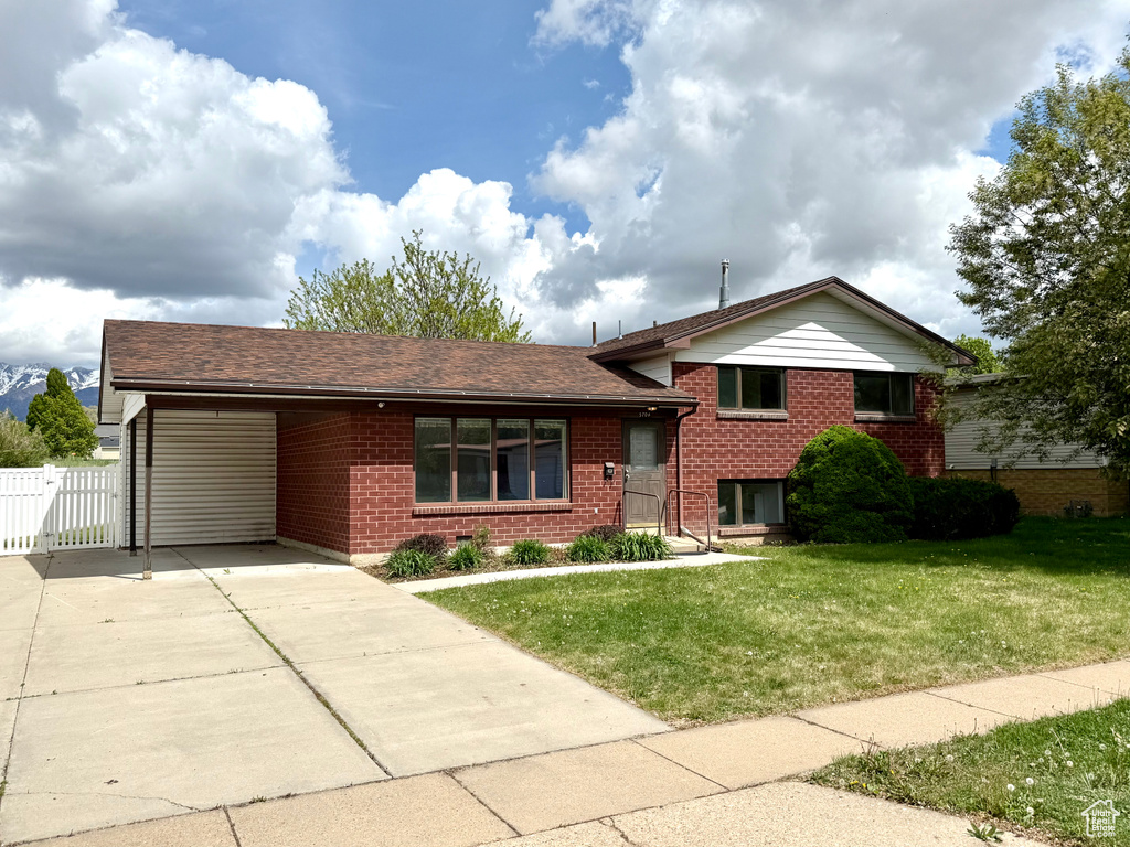Split level home featuring concrete driveway, brick siding, a gate, and a front lawn