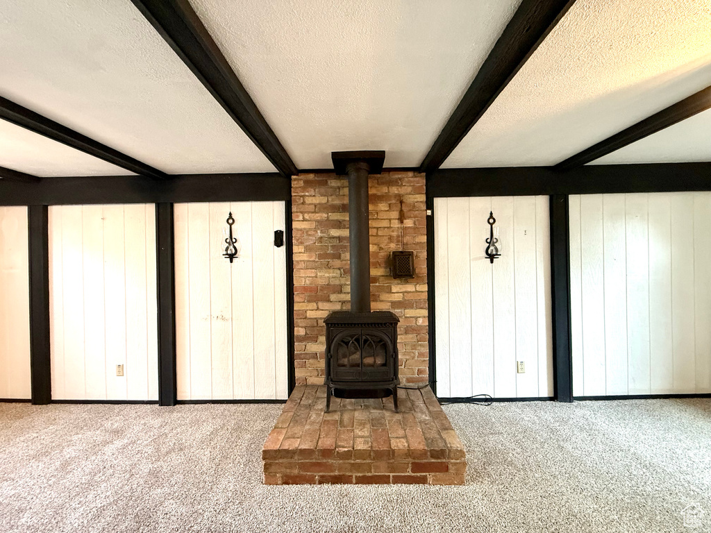 Unfurnished living room featuring a wood stove, a textured ceiling, beamed ceiling, and carpet