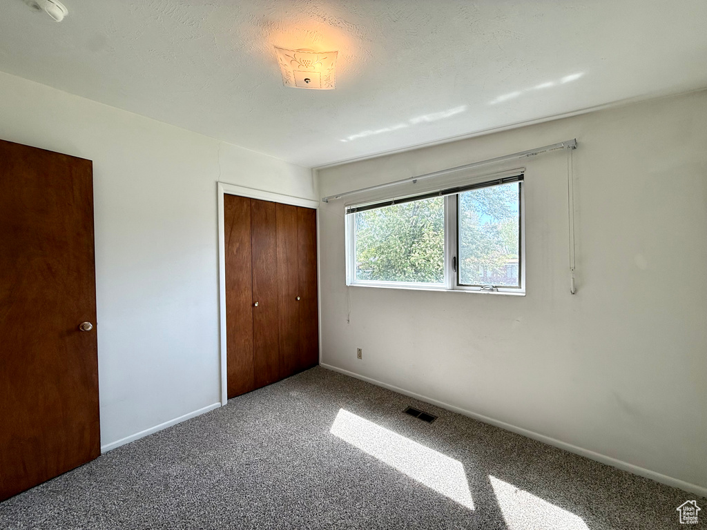 Unfurnished bedroom with carpet floors, baseboards, visible vents, and a closet