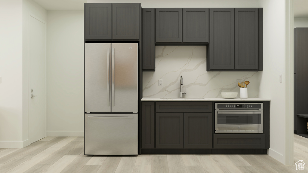 Kitchen featuring tasteful backsplash, a sink, freestanding refrigerator, light wood finished floors, and stainless steel oven