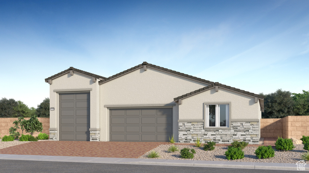 View of front of house with decorative driveway, an attached garage, fence, and stone siding