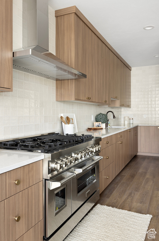 Kitchen featuring wall chimney range hood, a sink, light countertops, double oven range, and tasteful backsplash
