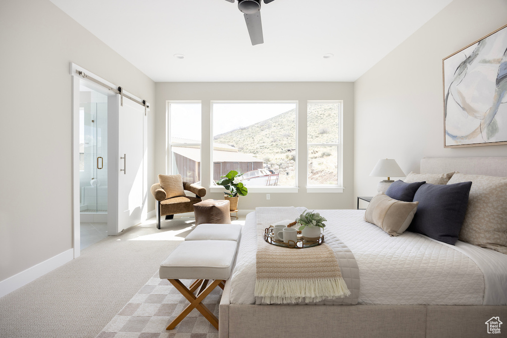 Carpeted bedroom featuring baseboards, ceiling fan, a barn door, and ensuite bathroom