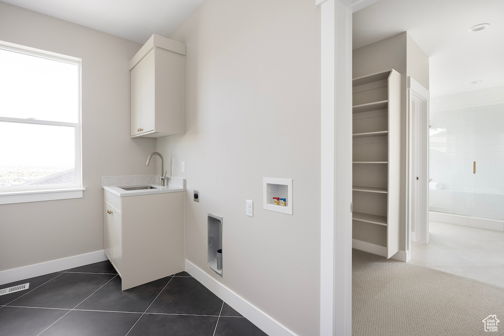 Clothes washing area with a sink, hookup for a washing machine, electric dryer hookup, dark tile patterned floors, and visible vents