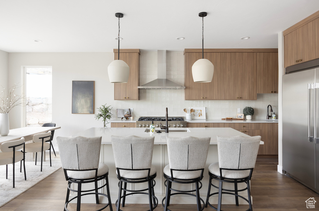 Kitchen with tasteful backsplash, modern cabinets, high quality fridge, wall chimney exhaust hood, and dark wood-type flooring