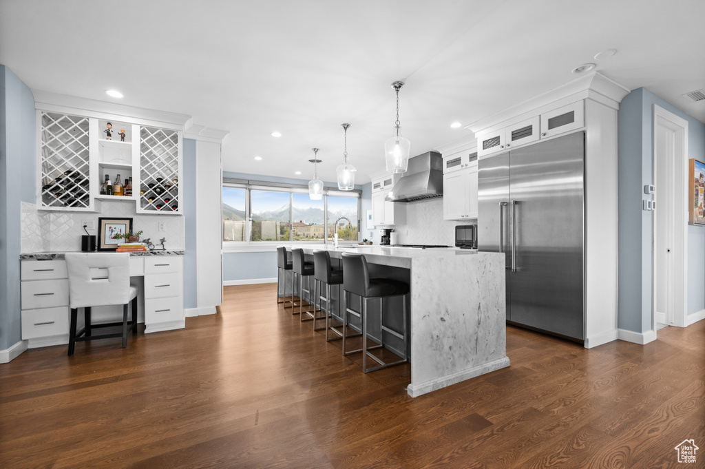 Kitchen featuring wall chimney range hood, recessed lighting, stainless steel built in refrigerator, and tasteful backsplash