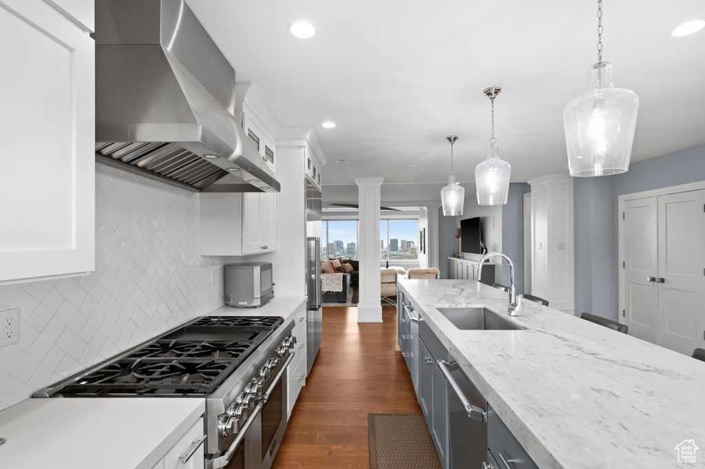 Kitchen with wall chimney range hood, stainless steel appliances, decorative columns, and a sink
