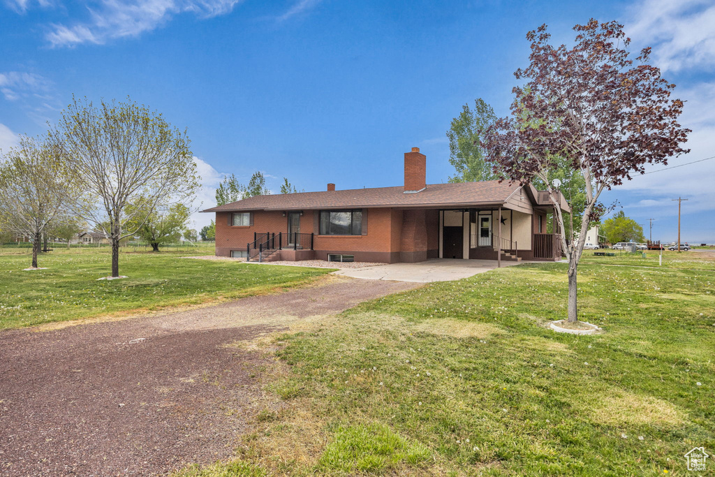 Single story home featuring an attached carport, a chimney, a front lawn, and aphalt driveway