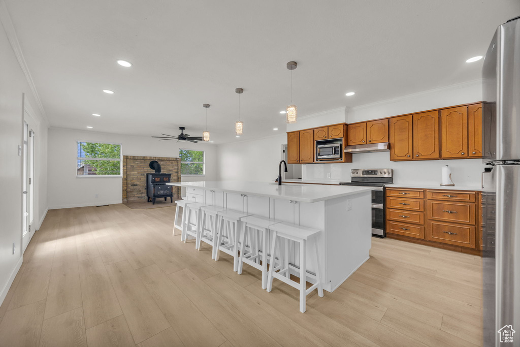 Kitchen featuring appliances with stainless steel finishes, a wood stove, brown cabinets, open floor plan, and under cabinet range hood