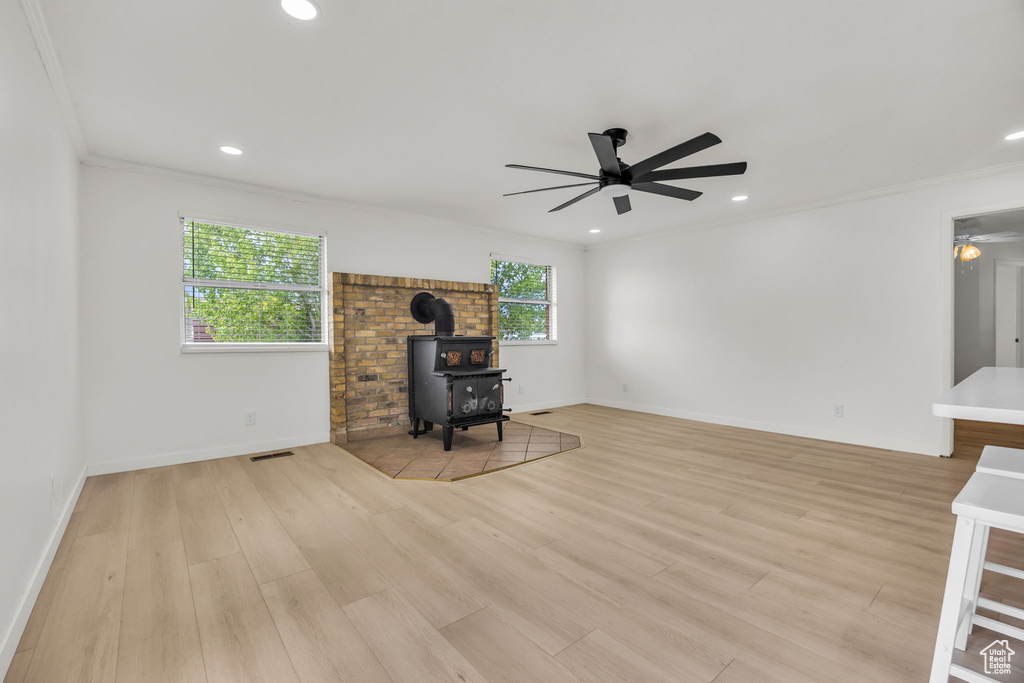Unfurnished living room with crown molding, ceiling fan, a wood stove, light wood-style floors, and visible vents