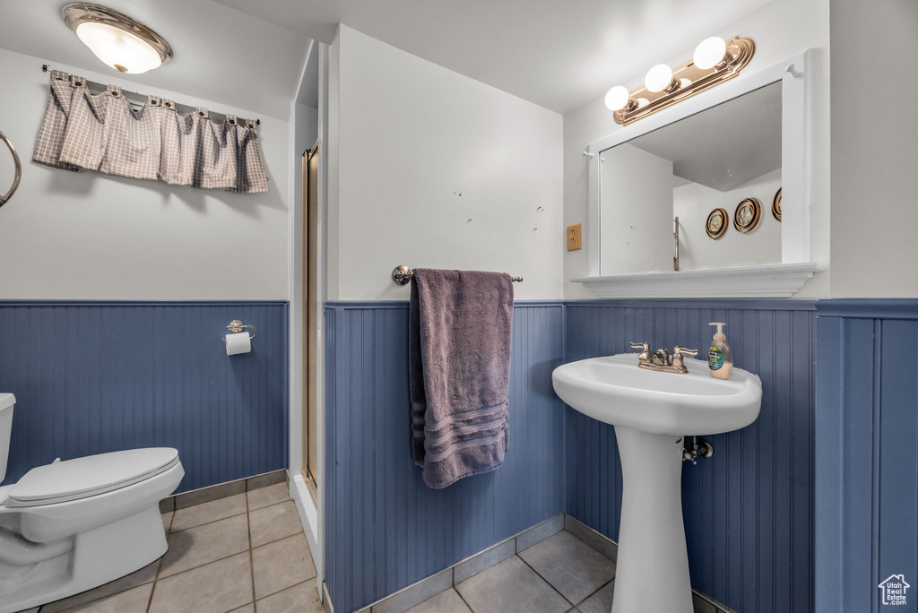 Bathroom featuring a shower with door, toilet, tile patterned floors, and a wainscoted wall