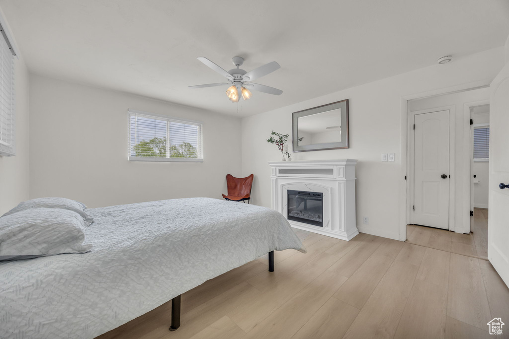Bedroom featuring a glass covered fireplace, ceiling fan, and light wood finished floors