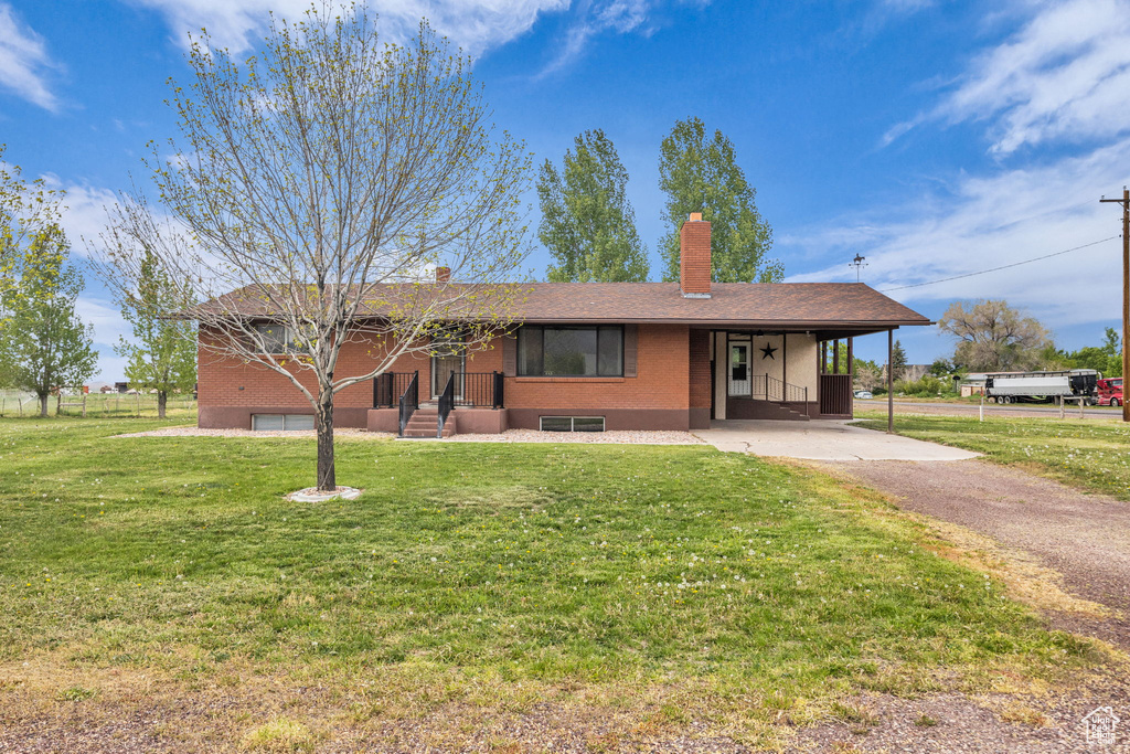 Ranch-style house featuring a front yard, a chimney, brick siding, driveway, and a carport