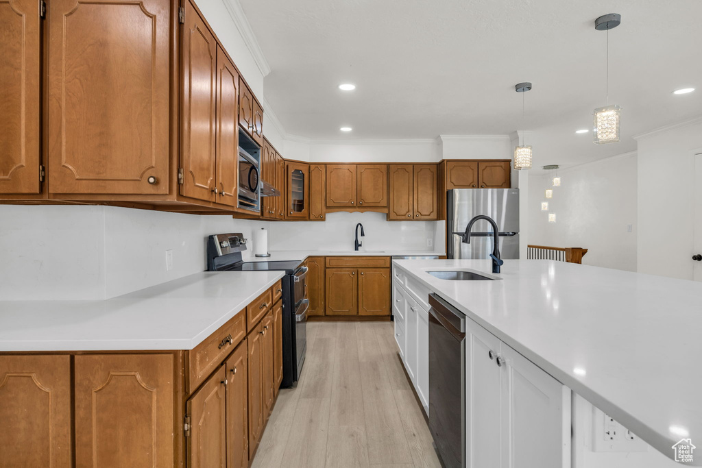 Kitchen with a sink, appliances with stainless steel finishes, brown cabinetry, and light wood-type flooring