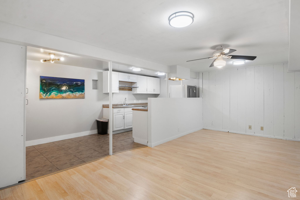 Kitchen featuring a peninsula, baseboards, white cabinets, a ceiling fan, and light wood-style flooring