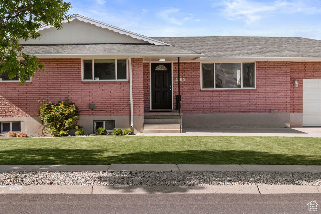 View of front of home with brick siding, a garage, a front yard, and roof with shingles