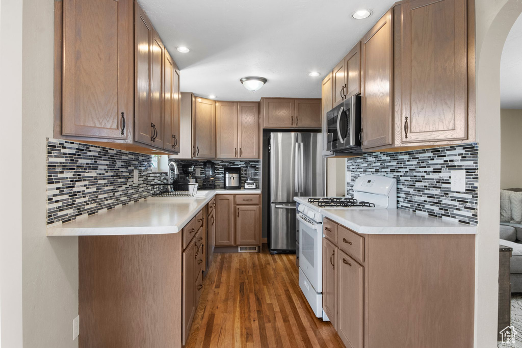Kitchen featuring arched walkways, wood finished floors, a sink, light countertops, and stainless steel appliances