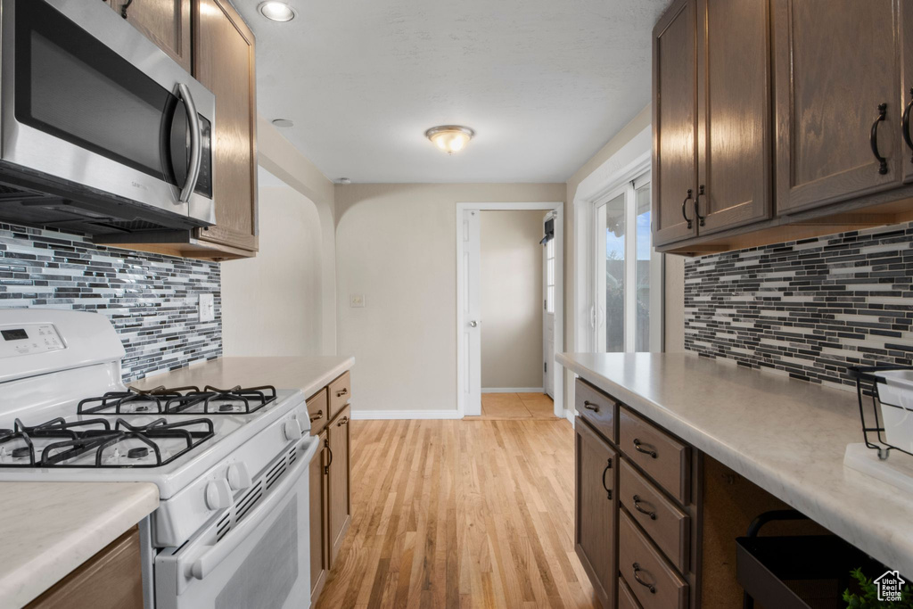 Kitchen with light countertops, decorative backsplash, stainless steel microwave, and gas range gas stove