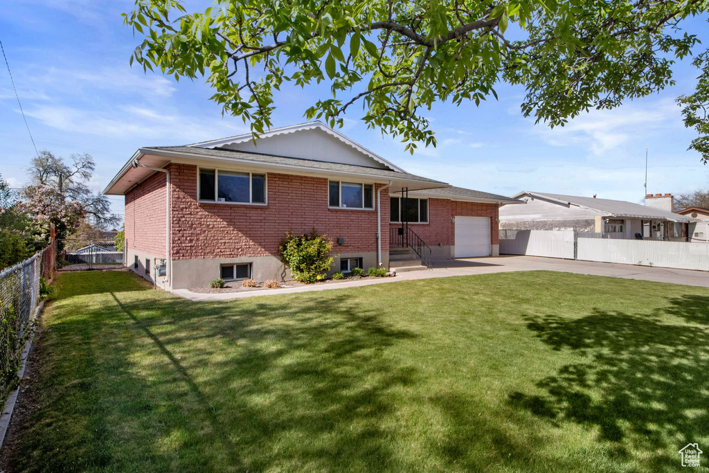 Back of house featuring fence private yard, a lawn, brick siding, concrete driveway, and an attached garage