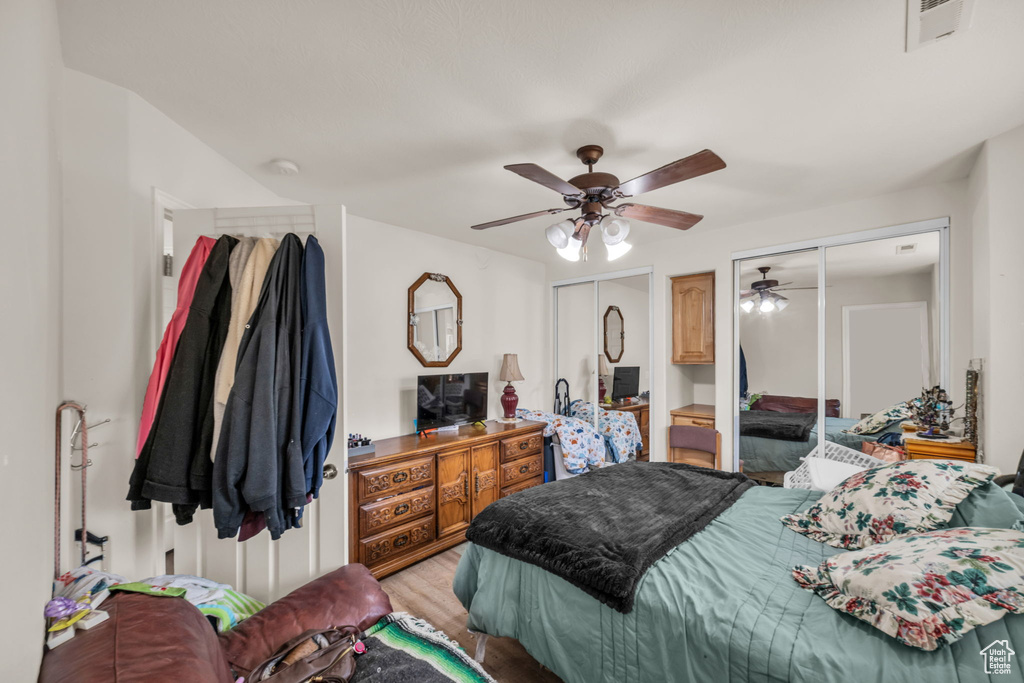 Bedroom featuring visible vents, light wood-style flooring, multiple closets, and a ceiling fan