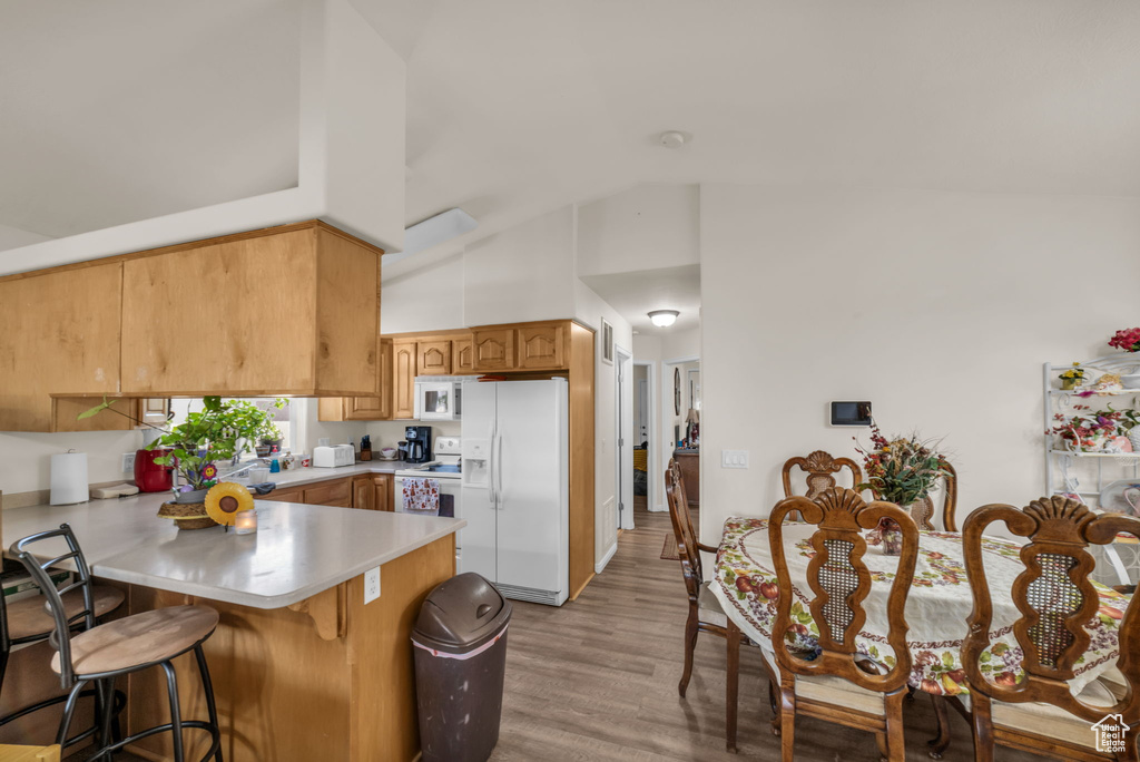 Kitchen featuring light countertops, high vaulted ceiling, a peninsula, white appliances, and light wood-style flooring