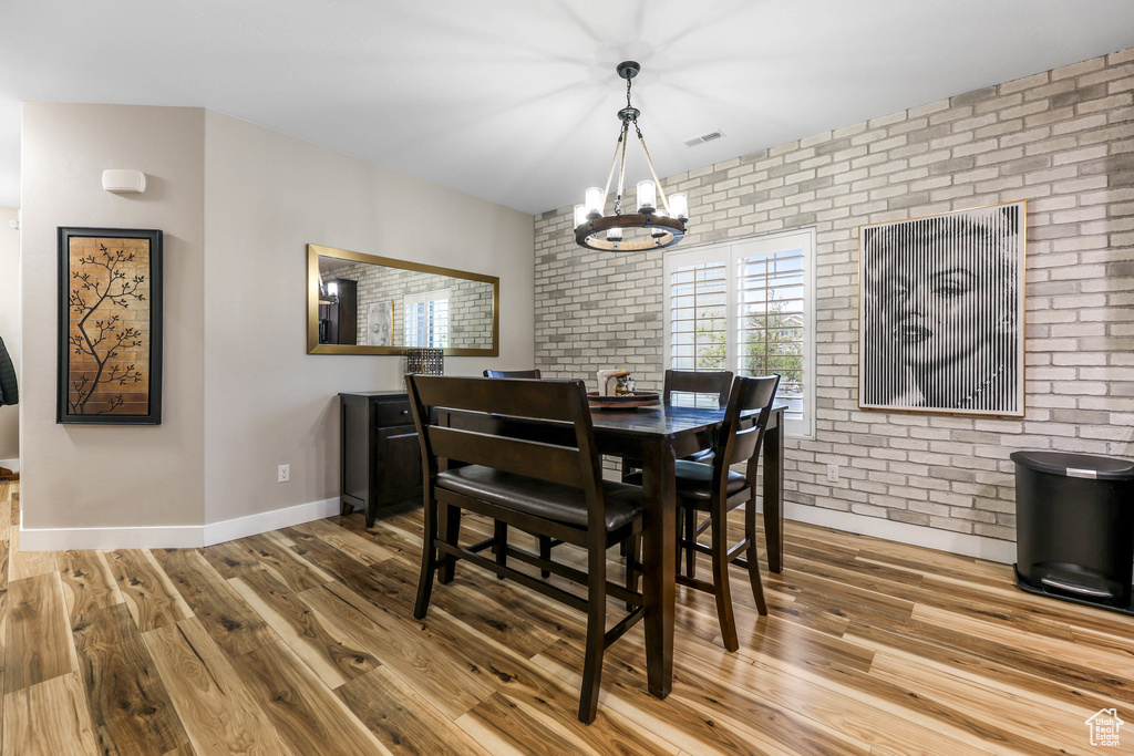 Dining space featuring brick wall, visible vents, wood finished floors, baseboards, and an inviting chandelier