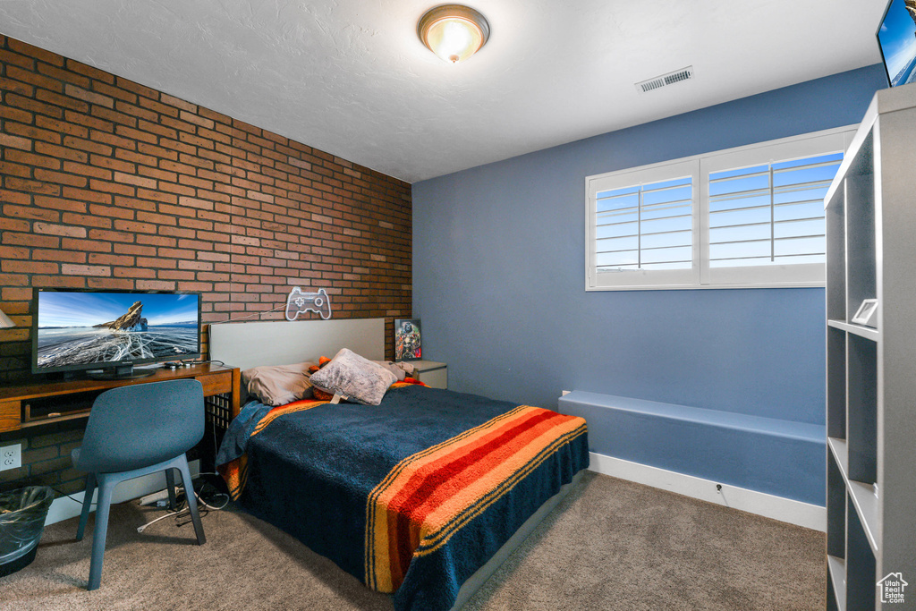 Bedroom with carpet flooring, brick wall, and visible vents