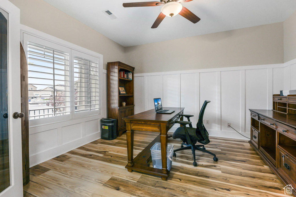 Office area with ceiling fan, a decorative wall, light wood-style flooring, and visible vents