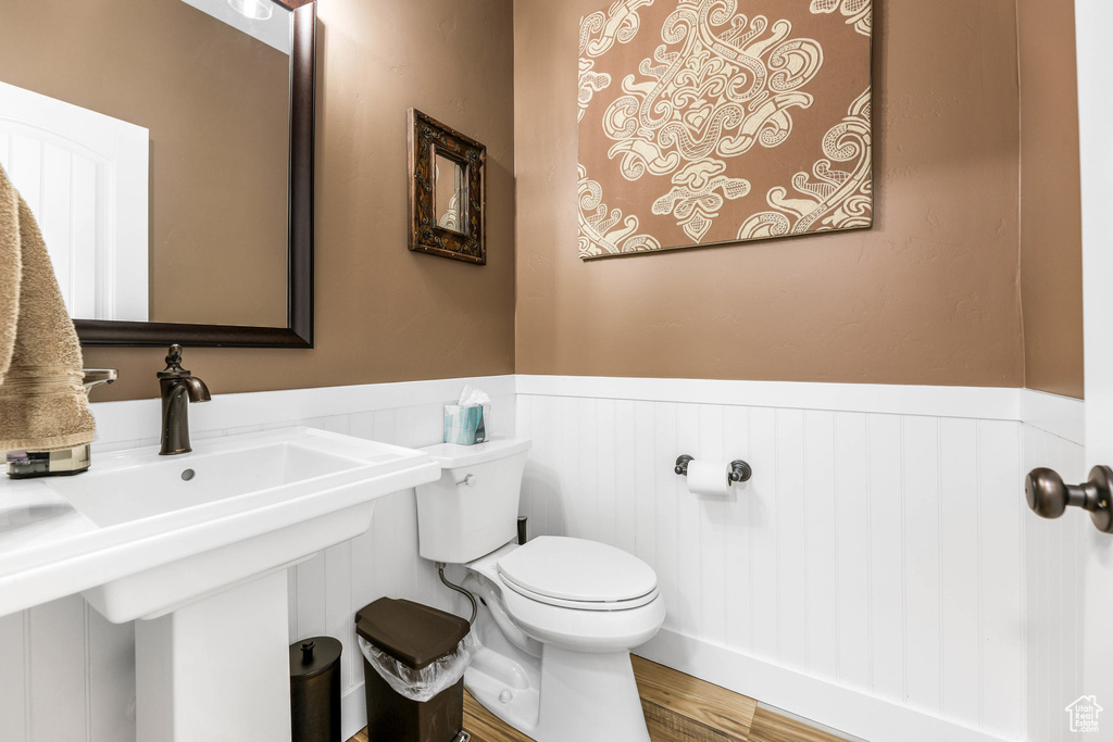 Half bath with a sink, wainscoting, toilet, and wood finished floors