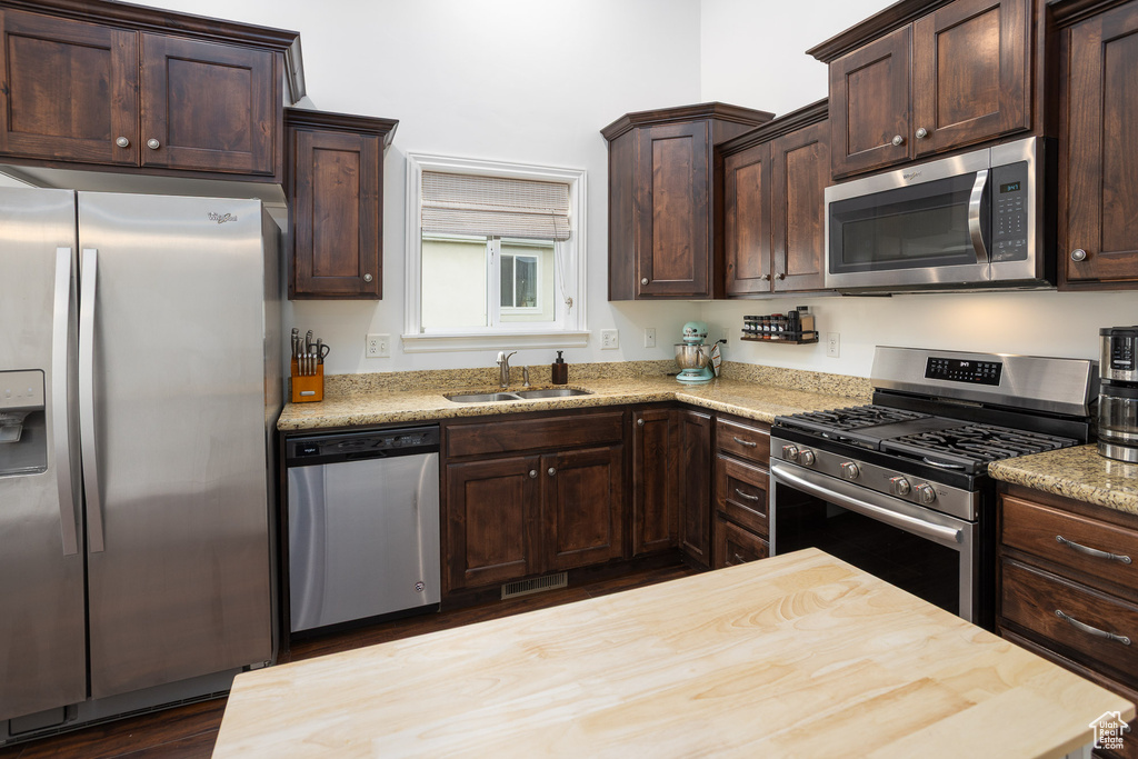 Kitchen featuring butcher block countertops, a sink, appliances with stainless steel finishes, and dark brown cabinetry