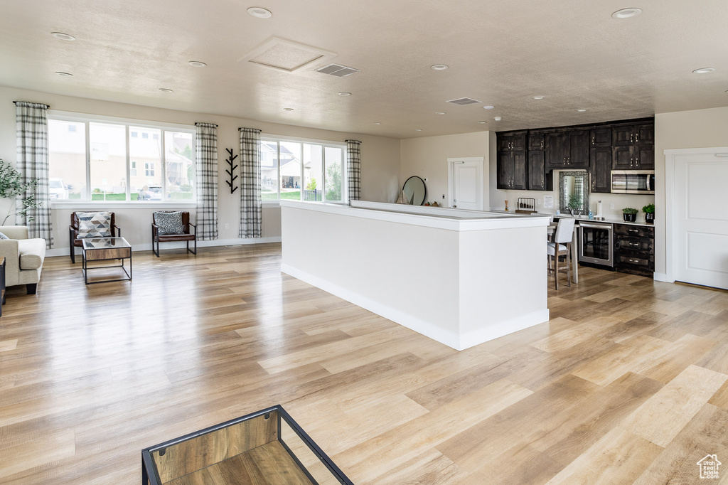 Kitchen featuring visible vents, light wood-type flooring, stainless steel microwave, beverage cooler, and open floor plan