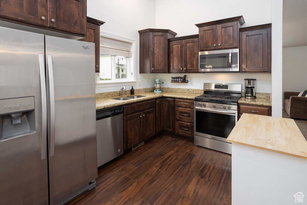 Kitchen with dark brown cabinets, butcher block countertops, a sink, dark wood finished floors, and appliances with stainless steel finishes