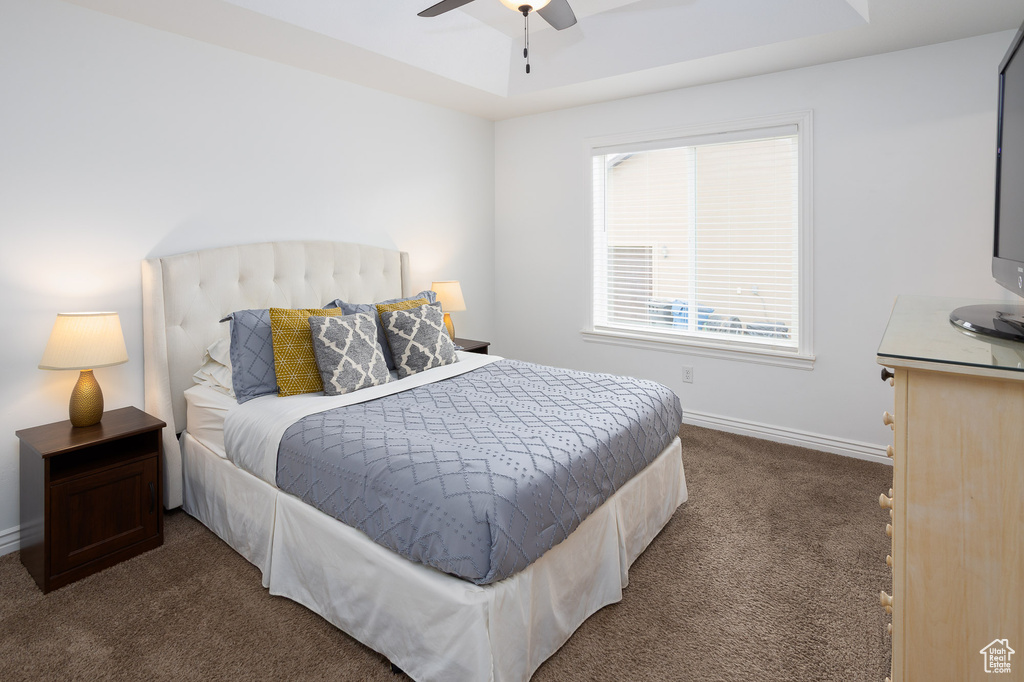 Bedroom featuring baseboards, a ceiling fan, a tray ceiling, and dark colored carpet