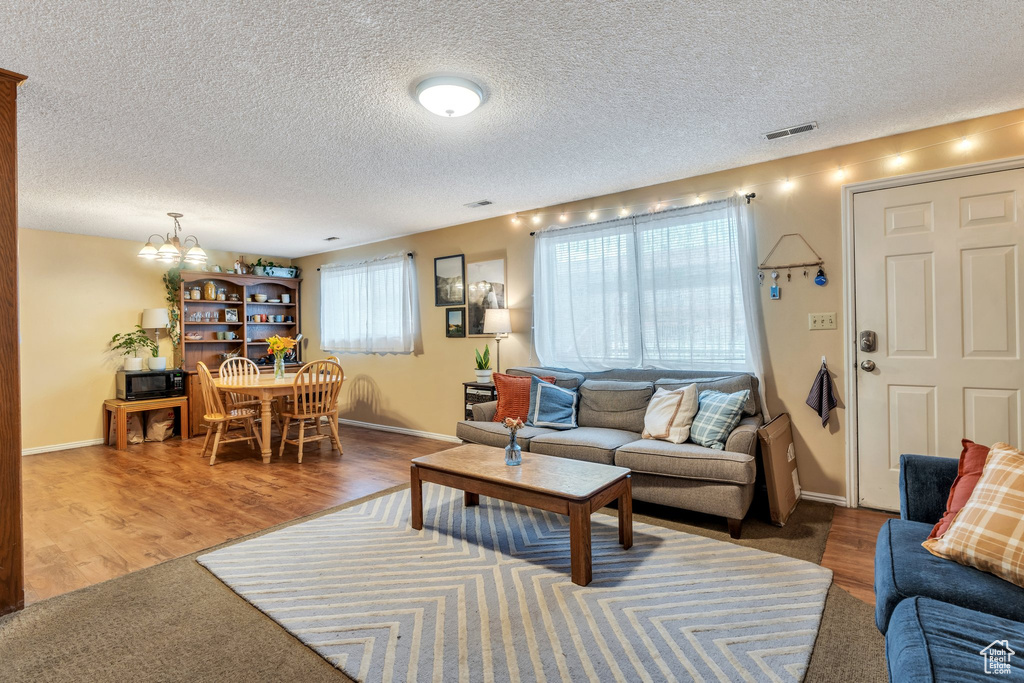 Living room featuring visible vents, a wealth of natural light, an inviting chandelier, and wood finished floors