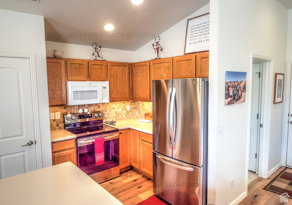 Kitchen featuring decorative backsplash, light countertops, lofted ceiling, light wood-style floors, and stainless steel appliances