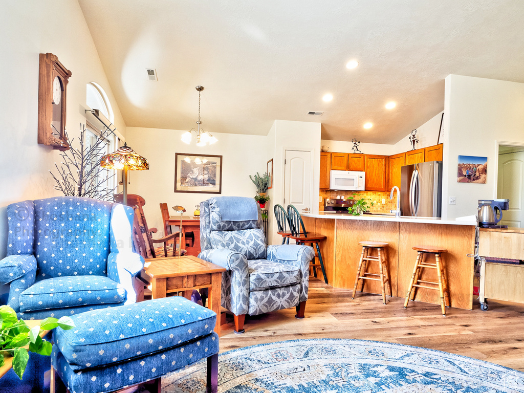Living room featuring a notable chandelier, recessed lighting, lofted ceiling, light wood-type flooring, and visible vents
