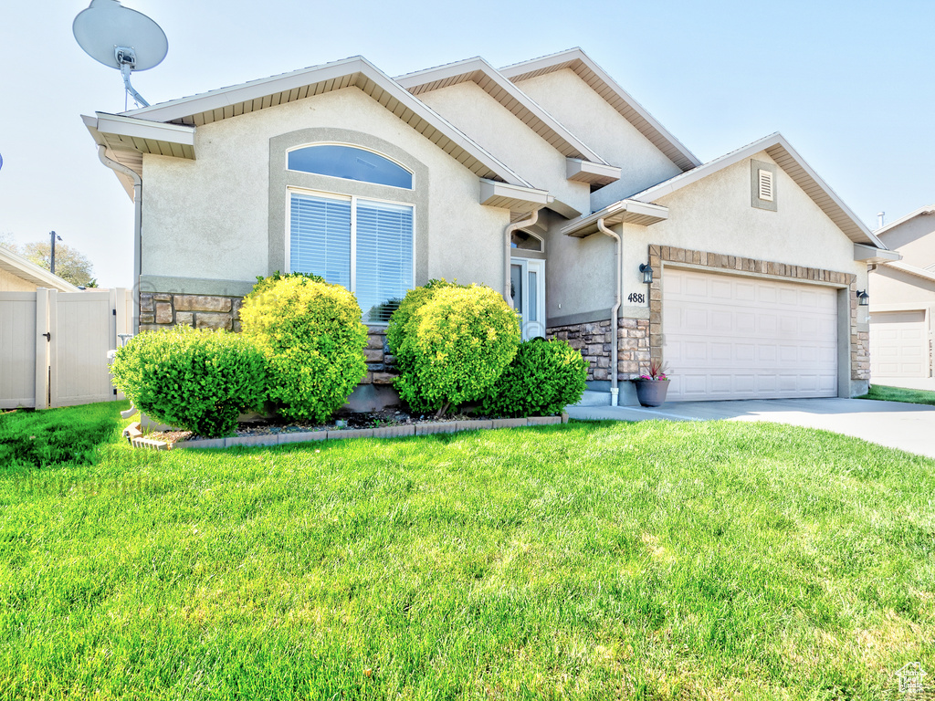 View of front of house with an attached garage, a front lawn, stucco siding, and stone siding