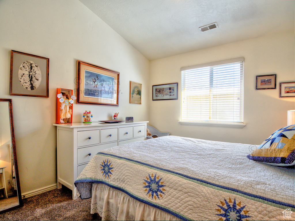 Bedroom with baseboards, visible vents, dark carpet, and lofted ceiling