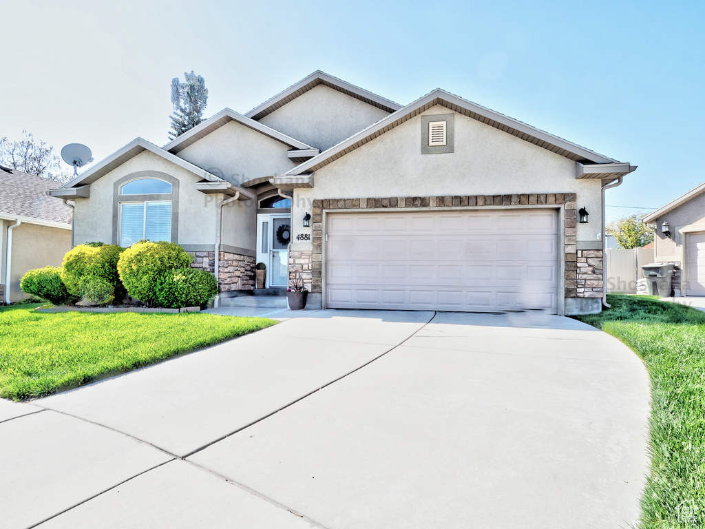 Ranch-style home featuring driveway, a garage, a front lawn, stone siding, and stucco siding