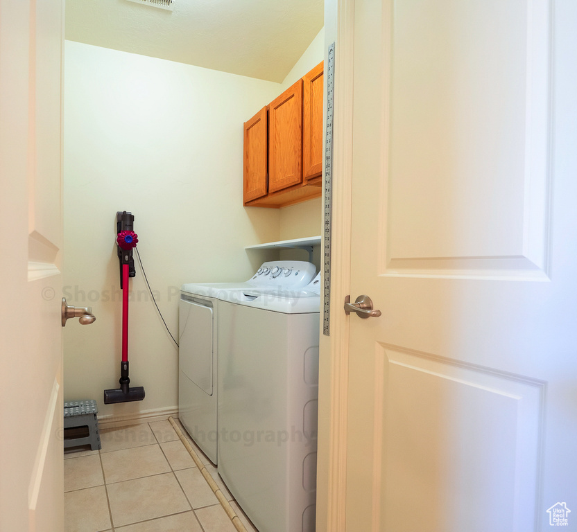 Laundry area with light tile patterned floors, separate washer and dryer, cabinet space, and visible vents