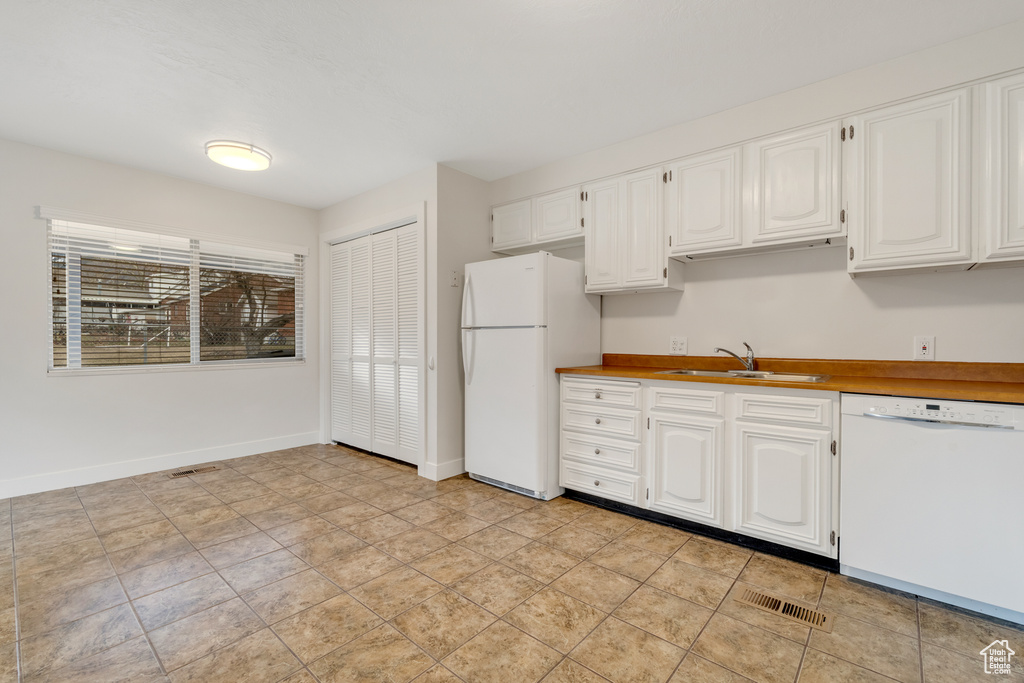 Kitchen with visible vents, a sink, baseboards, white appliances, and white cabinetry