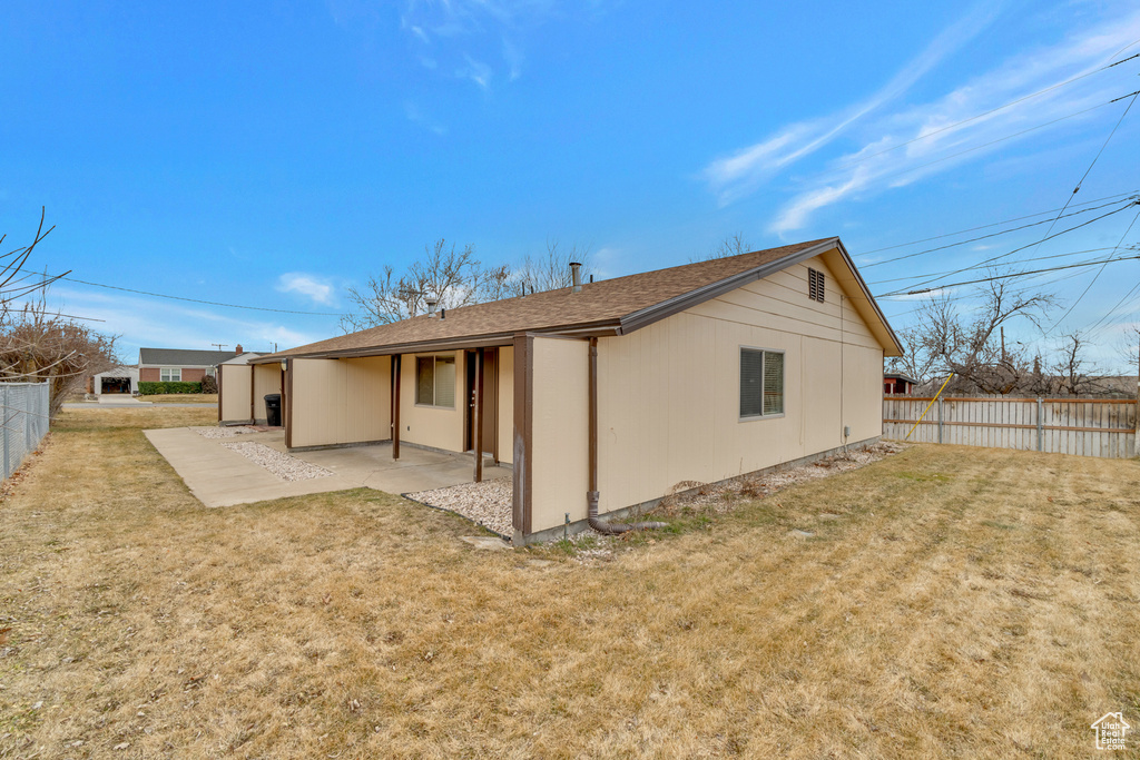 Rear view of house featuring a yard, roof with shingles, fence, and a patio area