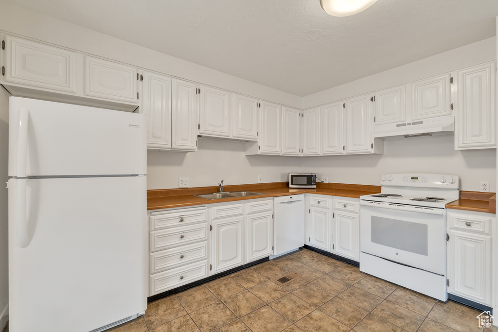 Kitchen featuring stone finish flooring, a sink, white cabinets, under cabinet range hood, and white appliances