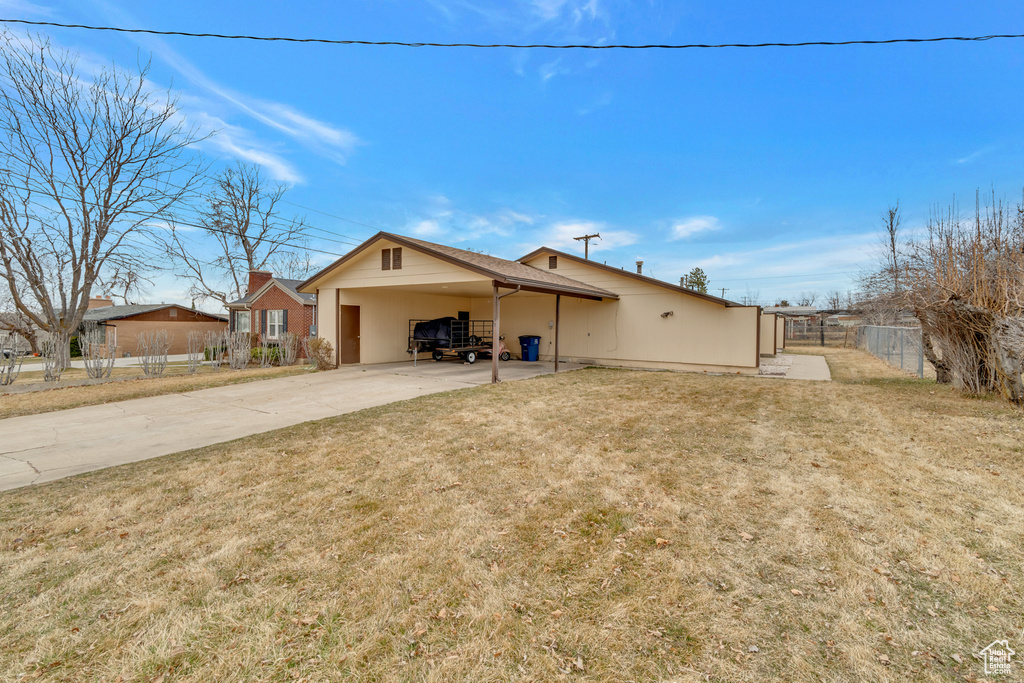 View of front facade featuring fence, a carport, concrete driveway, and a front lawn